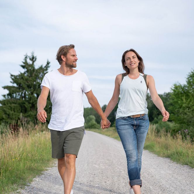 Ein Paar geht Hand in Hand auf einem Kiesweg durch eine grüne Landschaft spazieren.