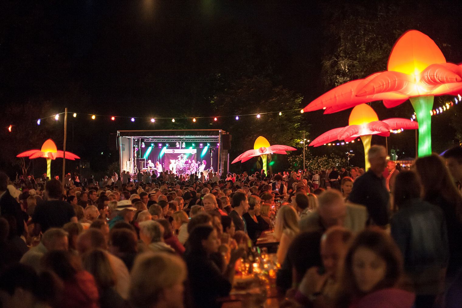 Stimmungsvoll beleuchtetes Festivalgelände mit Bühne und bunten Blumenlampen