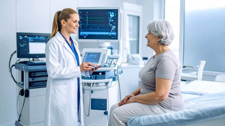  Ärztin berät ältere Patientin in moderner Arztpraxis