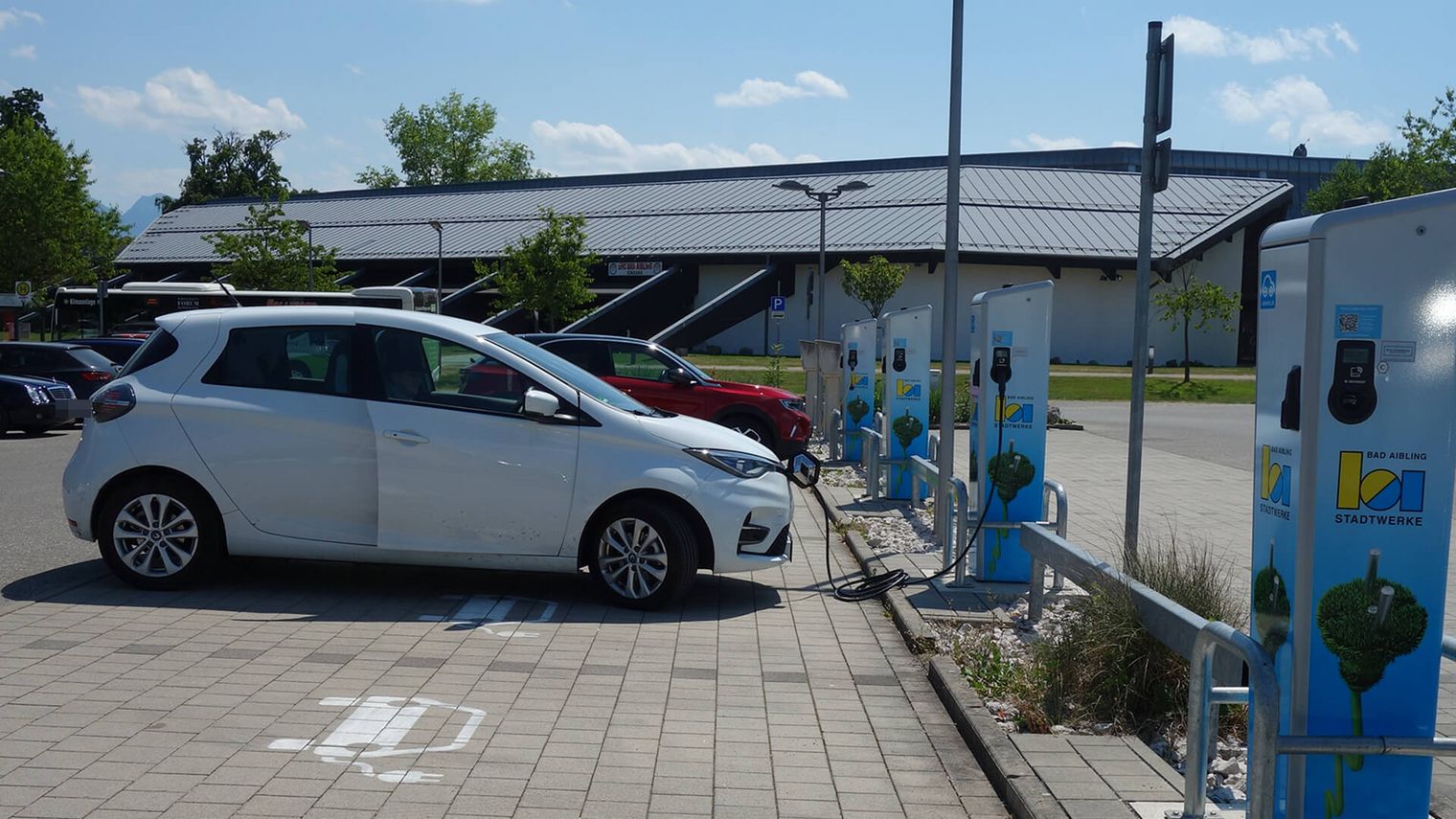 Ein weißes Elektroauto lädt an einer öffentlichen Ladestation vor der Therme Bad Aibling. Mehrere Ladepunkte der Stadtwerke Bad Aibling sind neben dem Fahrzeug sichtbar.