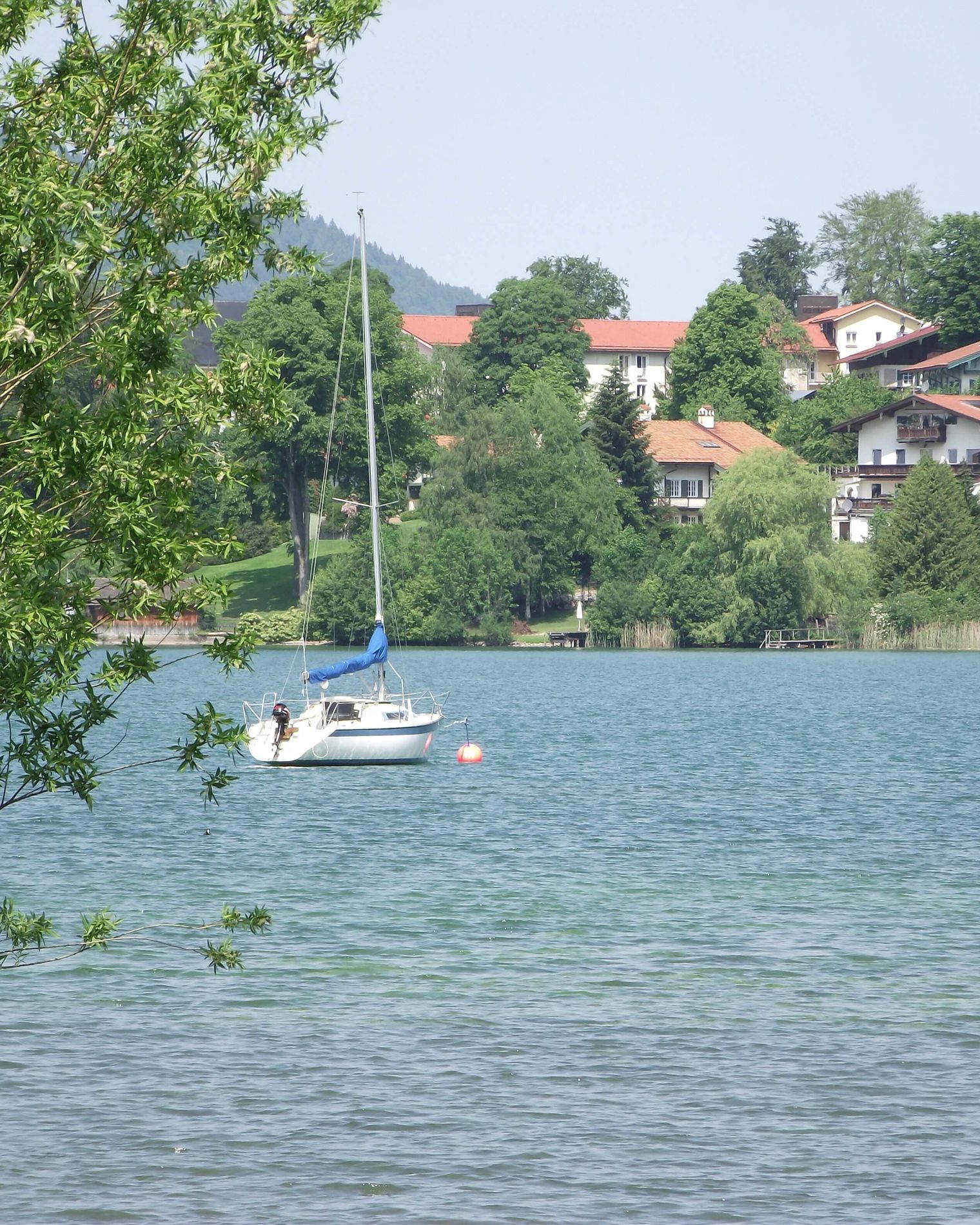 Eingefahrenes Segelboot schwimmt auf Tegernsee mit Häusern im Hintergrund