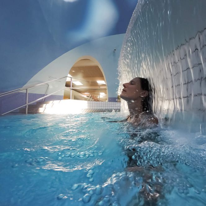 Frau entspannt im Thermalbecken der Therme Bad Aibling unter einem Wasserfall.