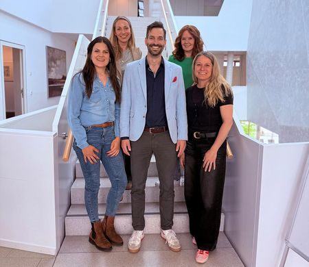 Fünf Personen stehen lächelnd auf einer Treppe in einem modernen Gebäude, passend zum Enjoy-your-business-Podcast.
