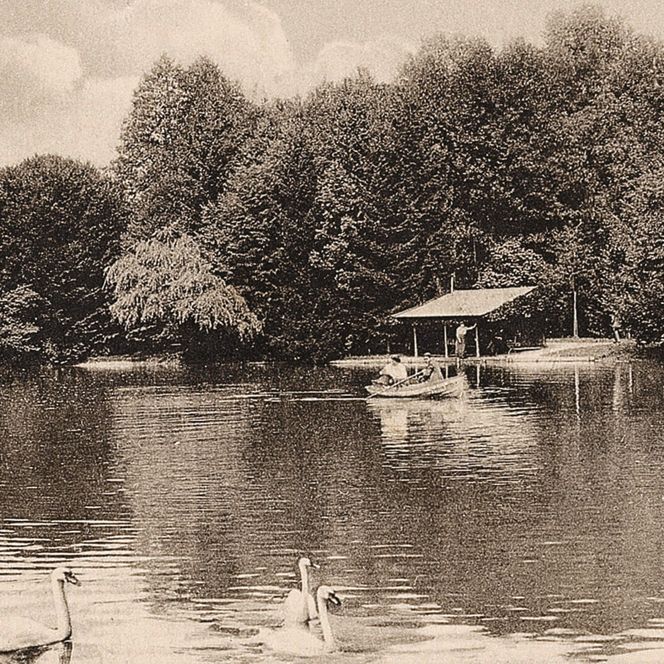 Historische Aufnahme des Irlachweihers im Kurpark mit Ruderbooten, Schwänen, Bootshaus und dichtem Baumbestand.