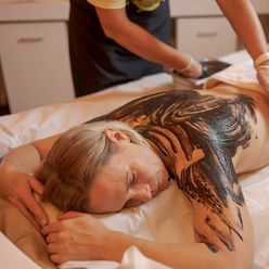 Eine Frau liegt entspannt auf einer Behandlungsliege, während ihr Rücken in der Therme Bad Aibling mit Moor bestrichen wird.