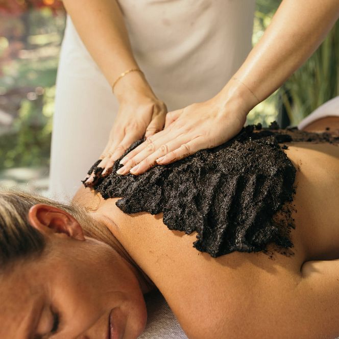 Therapeutin trägt Moorpackung auf den Rücken einer entspannt liegenden Frau bei einer Wellness- oder Gesundheitsbehandlung auf.