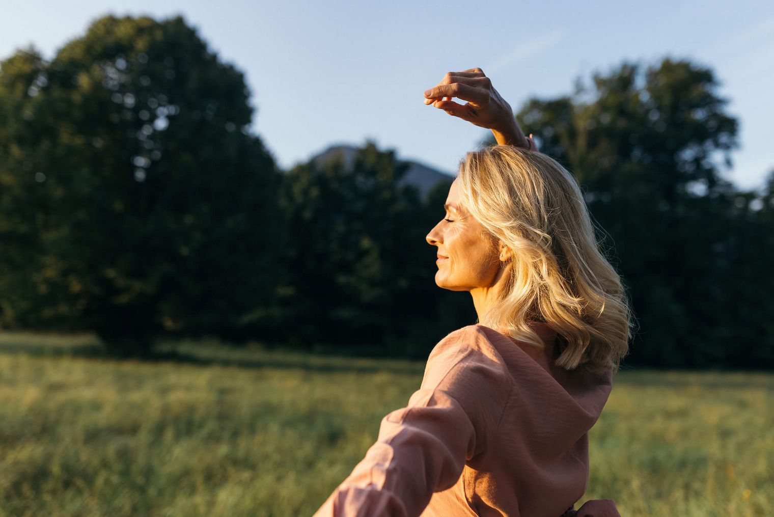 Eine Frau entspannt mit geschlossenen Augen auf einer Wiese in der Abendsonne.