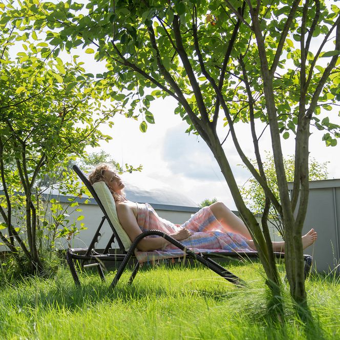 Eine Frau entspannt auf einem Liegestuhl im grünen Garten der Therme Bad Aibling.