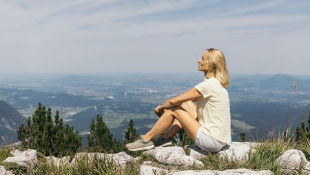 Eine Frau sitzt entspannt auf einem Berggipfel und blickt über die Landschaft in Bayern.
